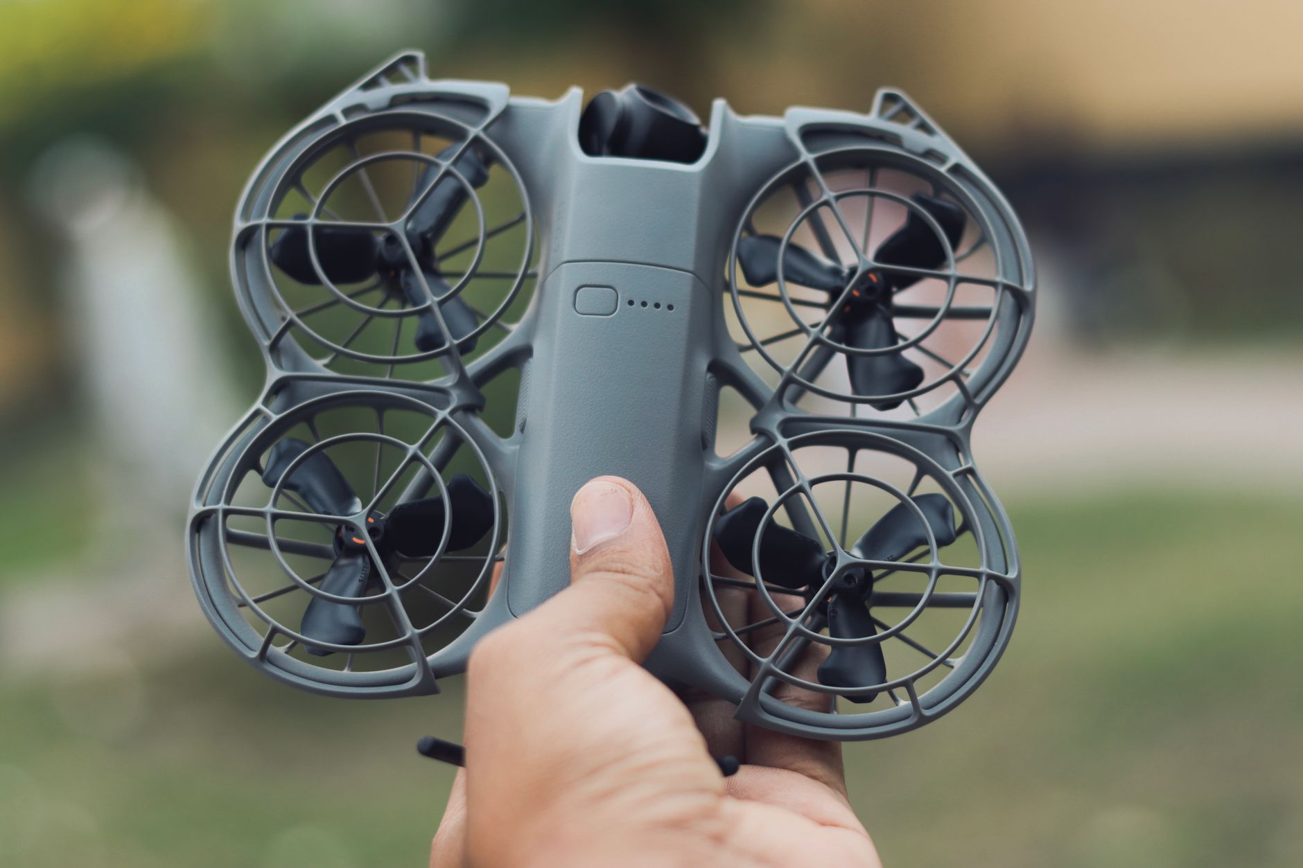 Two hands holding a compact grey folding camera drone above a grassy field