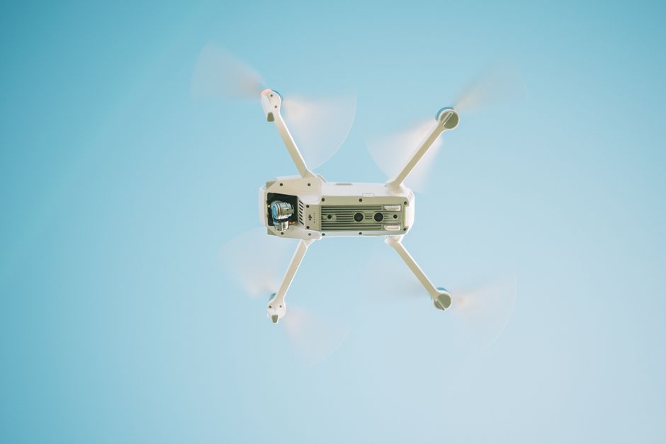 A white drone flying under a clear blue sky.